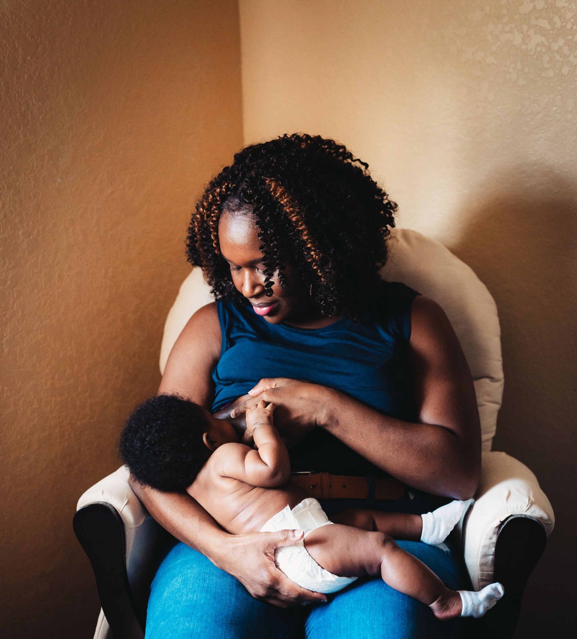African American woman breastfeeds her 3 month old baby at home, motherhood